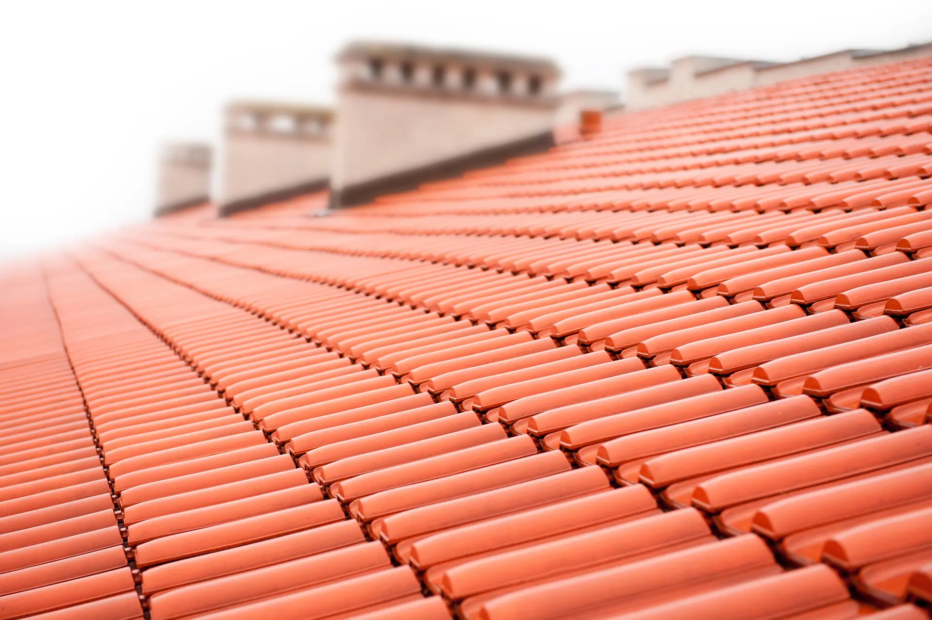 Overlapping rows of red roof tiles with chimneys maintained by Apex Roofing Services Bournemouth
